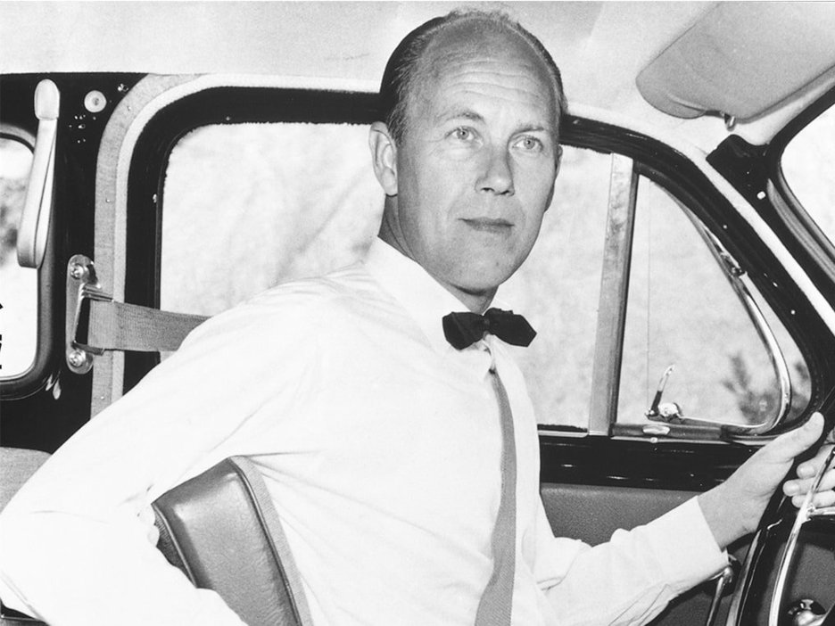 Zu sehen ist der Entwickler des Dreipunktgurtes Nils Ivar Bohlin. Er sitzt angeschnallt in einem Fahrzeug und gibt den Blick frei auf den Gurt um Brustkorb und Becken.