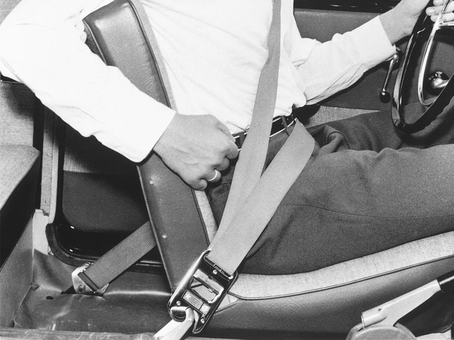 Zu sehen ist der Entwickler des Dreipunktgurtes Nils Ivar Bohlin. Er sitzt angeschnallt in einem Fahrzeug und gibt den Blick frei auf den Gurt um Brustkorb und Becken. Link zur vergrößerten Darstellung des Bildes.