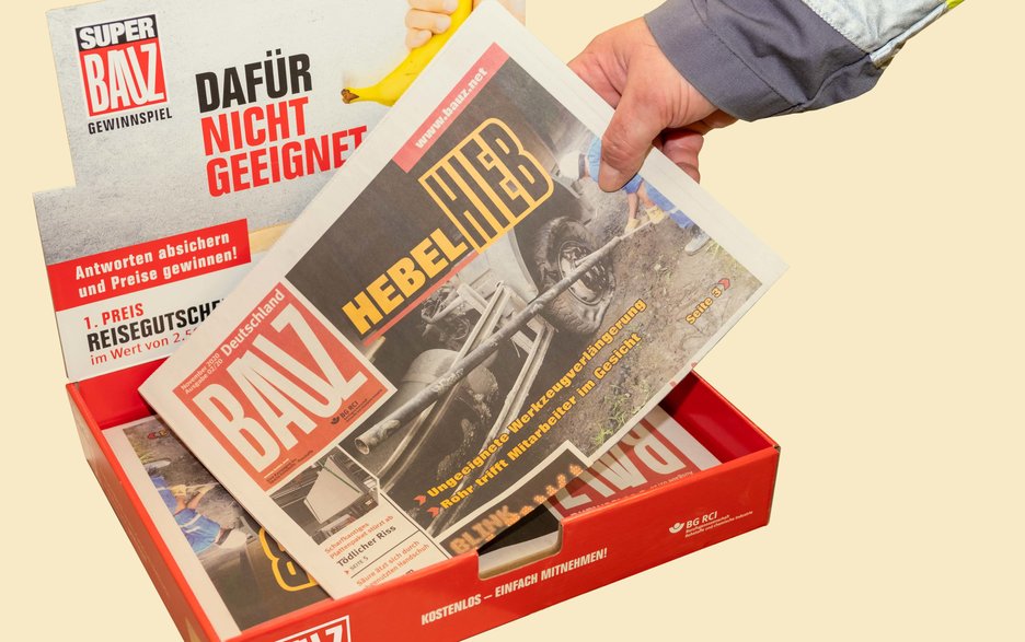 Das Bild zeigt einen BAUZ-Tresenaufsteller und eine Hand, die eine der darin liegenden BAUZ-Zeitungen nimmt.