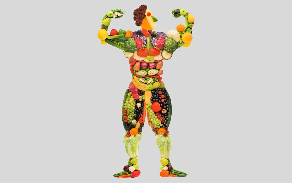 Auf dem Foto ist ein aus Obst und Gemüse geformter Mann zu sehen, der muskulös wirkt und vor Kraft strotzend beide Arme erhoben hat, um seine Muskeln zu zeigen.  Link zum Artikel.