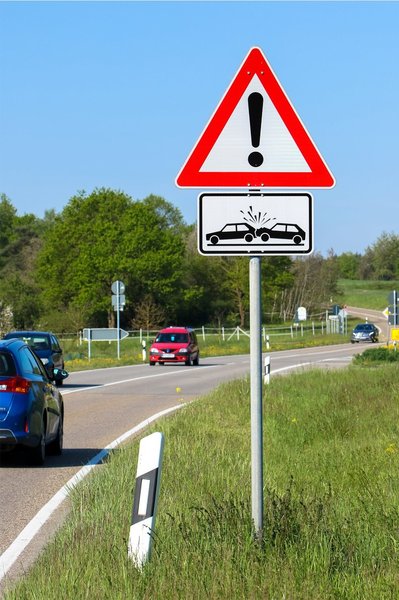 Ein Verkehrsschild auf einer kurvigen Landstraße warnt vor Auffahrunfällen an einer Einbiegung rechts und links.
