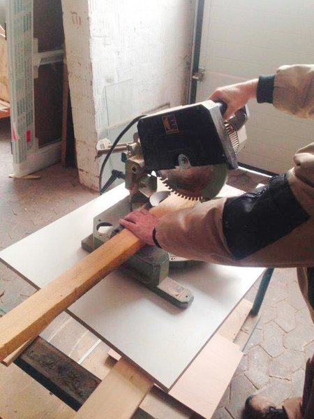 Das Bild zeigt, wie ein Mitarbeiter den Handgriff einer Kappsäge in der rechten Hand führt, während er mit der linken ein Holzbrett festhält. 