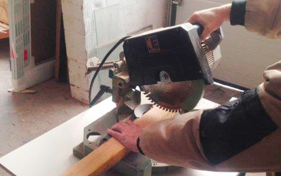 Das Bild zeigt, wie ein Mitarbeiter den Handgriff einer Kappsäge in der rechten Hand führt, während er mit der linken ein Holzbrett festhält.  Link zum Artikel.