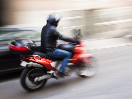 Das Foto zeigt einen Mann mit Motorradhelm und Lederjacke, der schnell auf einem roten Motorrad fährt. Die Geschwindigkeit wird mittels Unschärfe im Bild dargestellt. Dieses steht symbolhaft für das Fahren mit überhöhter Geschwindigkeit bei Zweiradfahrern. Link zur vergrößerten Darstellung des Bildes.