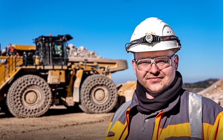 Das Bild zeigt den Mitarbeiter Daniel Koch auf dem Betriebsgelände der Fels-Werke. Im Hintergrund sind die Großgeräte zu sehen, mit denen er als Sicherheitsbeauftragter und Großgerätefahrer täglich zu tun hat. Link zur vergrößerten Darstellung des Bildes.