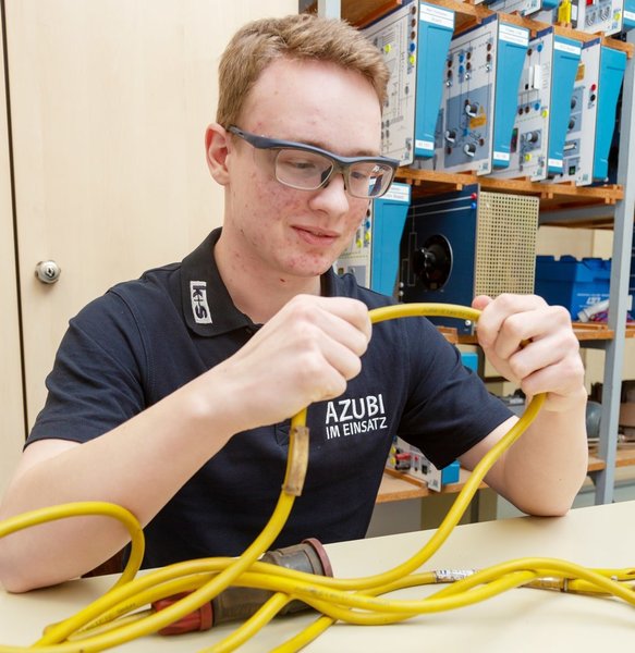 Der Auszubildende zum Chemikanten Timo Weß untersucht in der Lehrwerkstatt ein langes, elektrisches Kabel auf Schäden und Mängel.