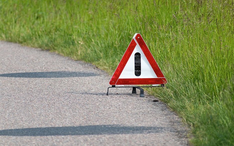 Auf der Landstraße steht ein Warndreieck. Es weist auf ein Auto hin, das mitten auf der Straße liegengeblieben ist, weil es eine Panne hat. Link zum Artikel.