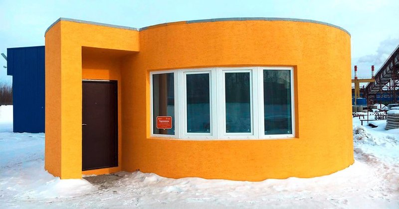 Das Bild zeigt ein orangefarbenes Betonhaus mit runden und eckigen Formen, das durch einen 3D-Drucker erschaffen wurde.